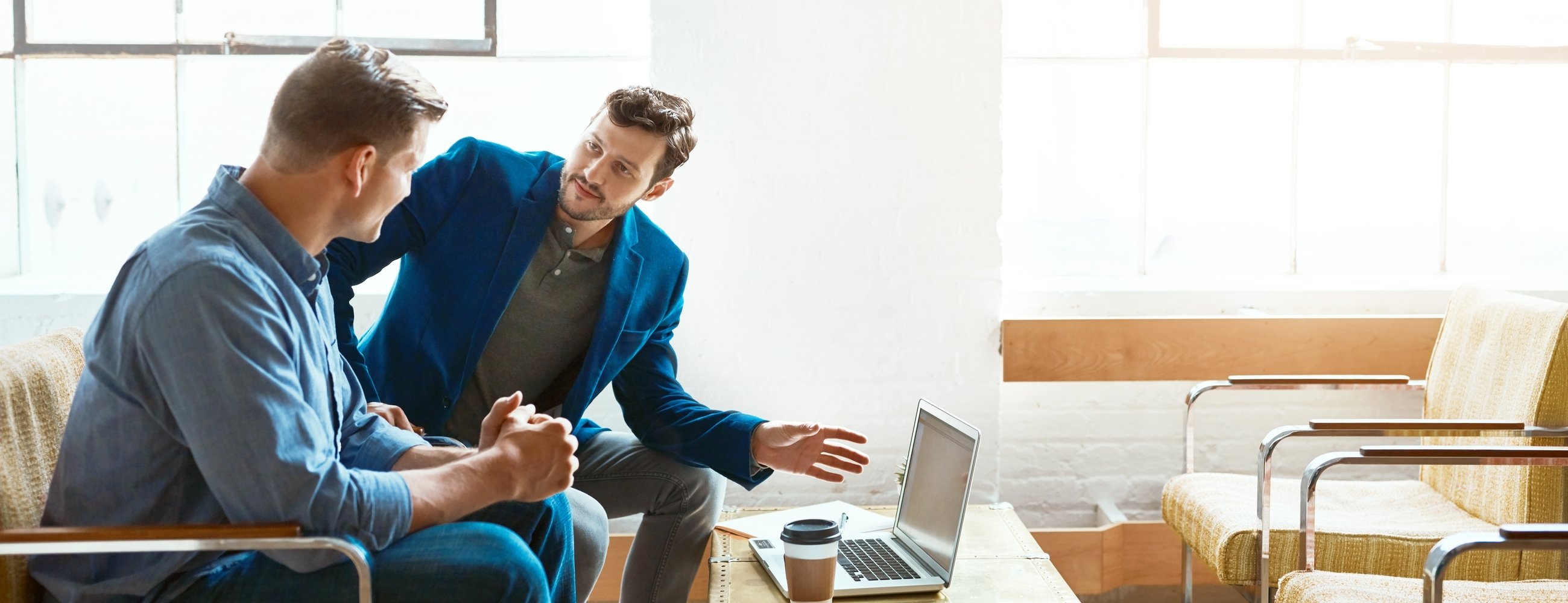 Shot of two young businessmen having a discussion and using a laptop together in a modern office